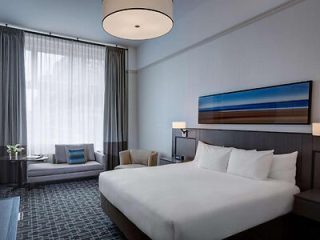 A modern hotel bedroom with a large bed, plush headboard, and a seating area by the window.